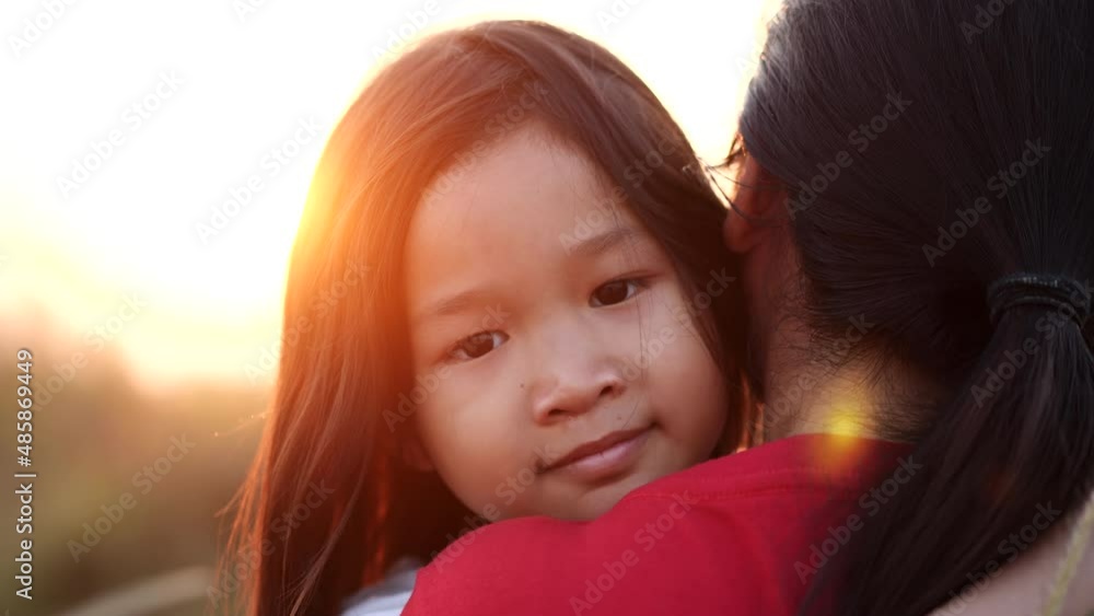 Close-up portrait Asian little child girl embrace or hugging mother, happy, smiling in beautiful nature outdoor sunset or sunshine, slow motion. Concept of love, happy family, mother, kid, summer.