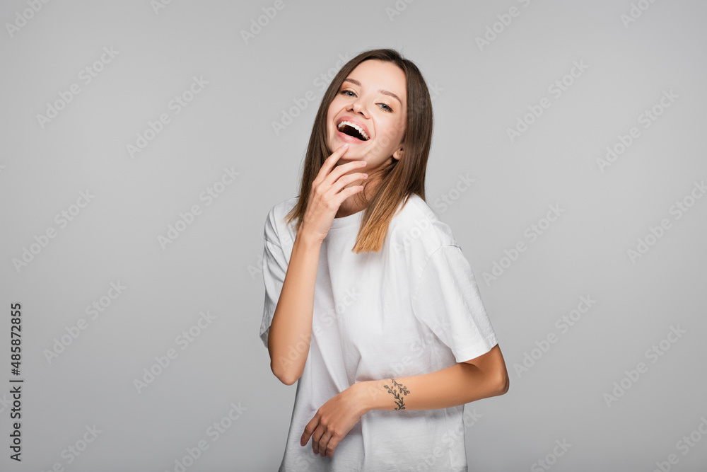 excited woman in white t-shirt laughing while looking at camera isolated on grey excited woman in white t-shirt laughing while looking at camera isolated on grey