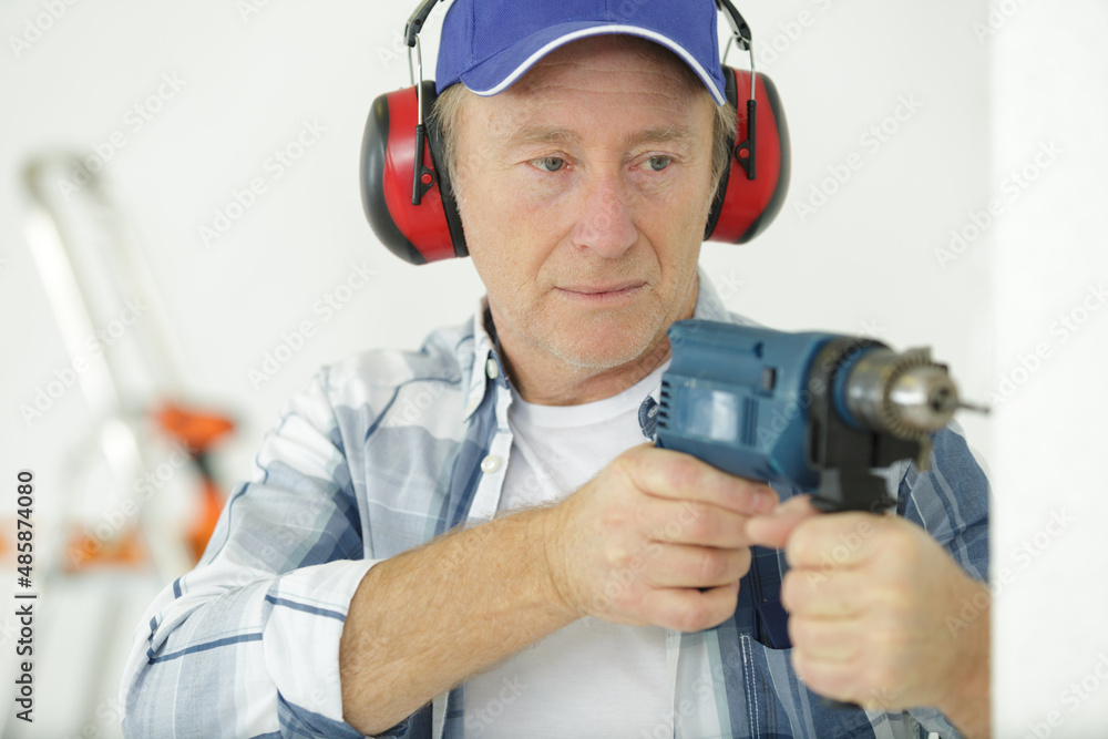 senior workman using drill and wearing ear-defenders senior workman using drill and wearing ear-defenders