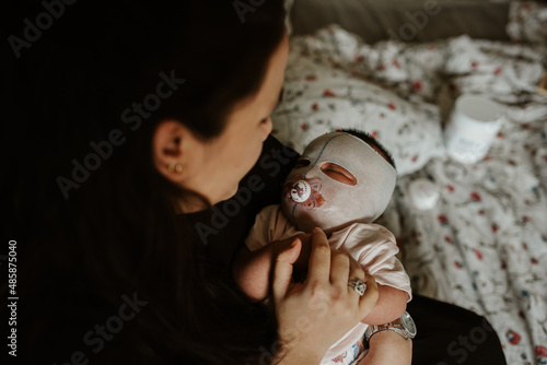 Mother looking at her newborn girl with eczema face mask
