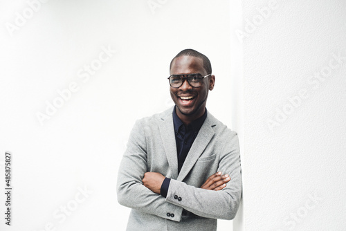 handsome african american businessman smiling with eyeglasses leaning against white wall
