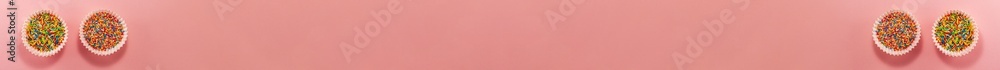Banner of four cupcake liners with colored sugar inside from above. Flat lay top view. Confectionery cooking concept on bright pink paper background. National cooking day Banner of four cupcake liners with colored sugar inside from above. Flat lay top view. Confectionery cooking concept on bright pink paper background. National cooking day