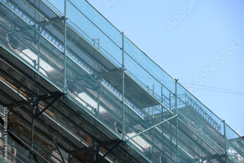 Building facade under renovation works with construction scaffolding frame covered with protective net for workers safety