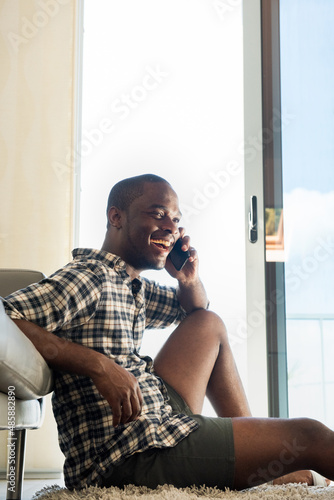 happy black man sitting at home talking with cellphone