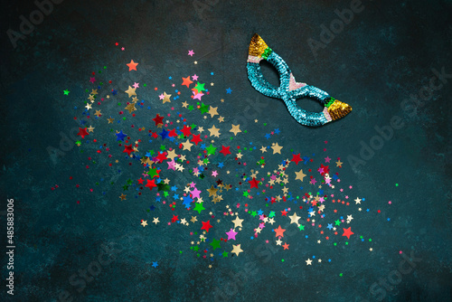 Carnival mask and varicolored glitter confetti. Top view, Close up on blue background