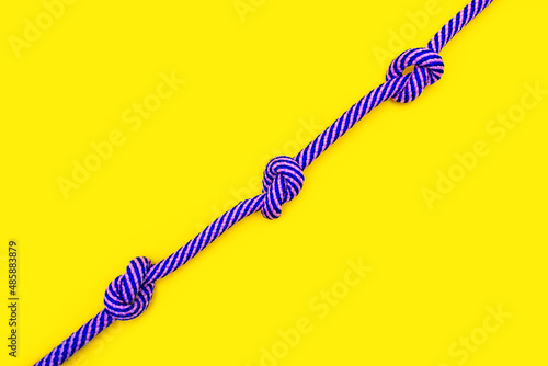 Multicolored rope with three knots on a yellow background. A strong blue-pink rope with knots in the center of a yellow background placed diagonally with free space for advertising or text