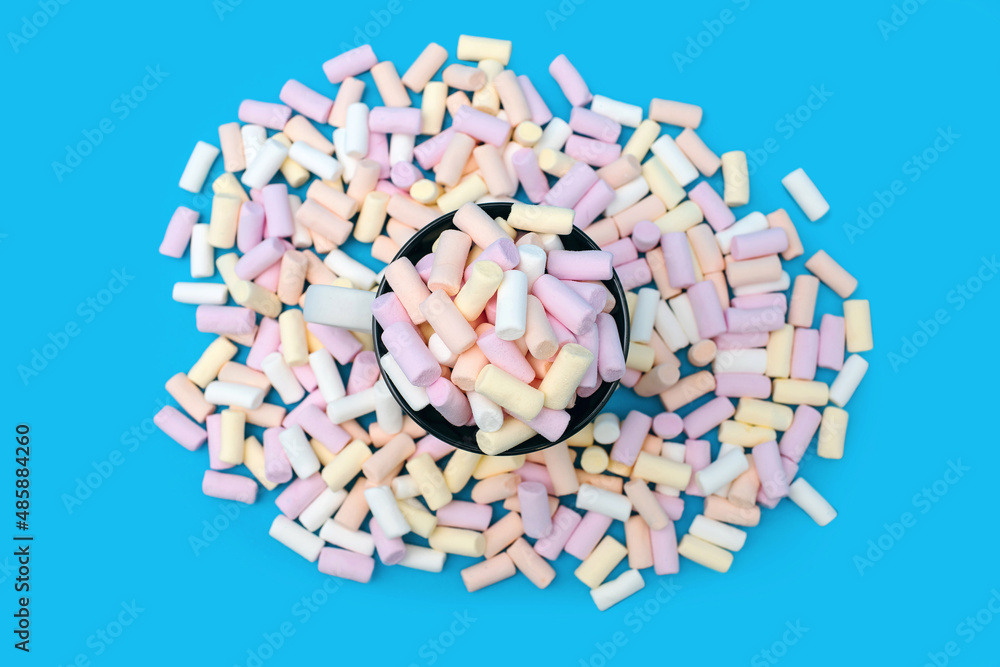 A mug with cocoa or hot chocolate and a lot of colorful marshmallows scattered on a blue background top view. A sweet airy dessert or addition to hot drinks in the form of cocoa