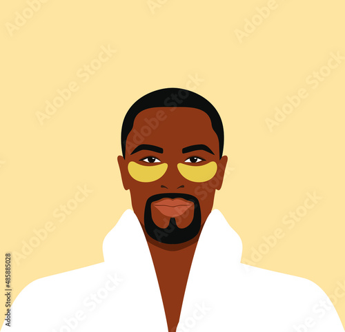 Bearded african man in a white bathrobe with gold eye patches on his face. Daily skincare routine