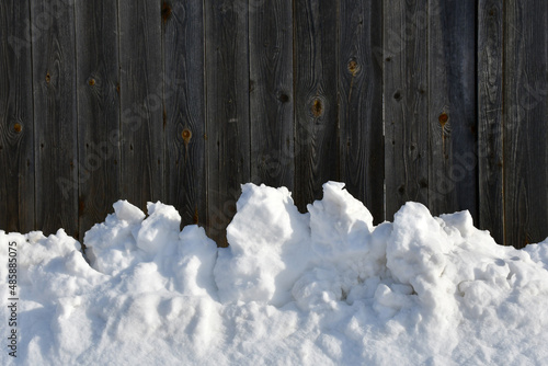 Winter background. A snowdrift on the background of an old fence made of unpainted boards. Lumps of snow. Wood texture