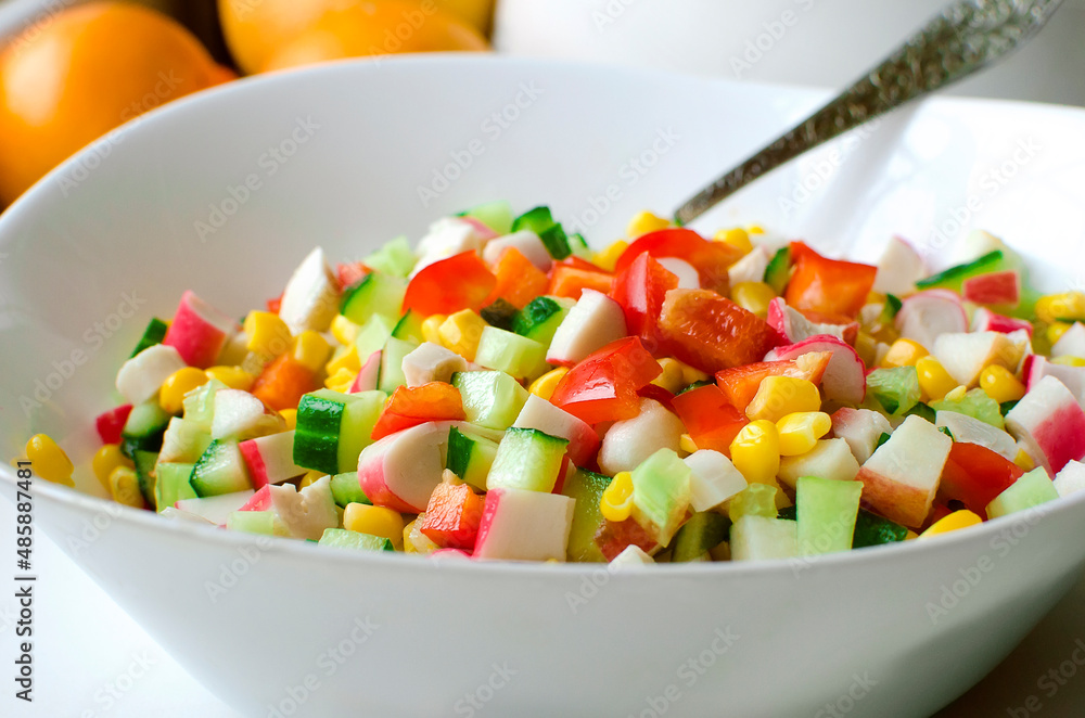 salad of fresh vegetables - cucumbers, bell peppers, corn and crab sticks in a white bowl on the table. salad of fresh vegetables - cucumbers, bell peppers, corn and crab sticks in a white bowl on the table.