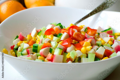 salad of fresh vegetables - cucumbers, bell peppers, corn and crab sticks in a white bowl on the table.