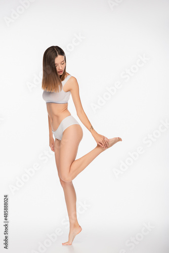 full length view of fit woman in underwear touching leg on white background