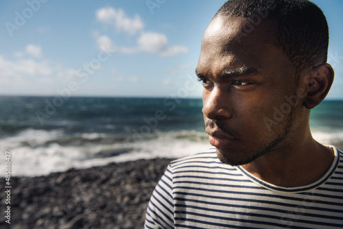 Close up handsome black man standing by water staring