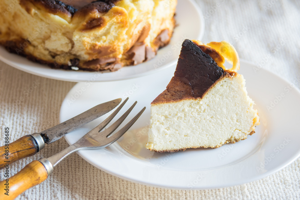 Basque Burnt San Sebastian Cheesecake with cutted piece on a white plate on light background, selective focus Basque Burnt San Sebastian Cheesecake with cutted piece on a white plate on light background, selective focus