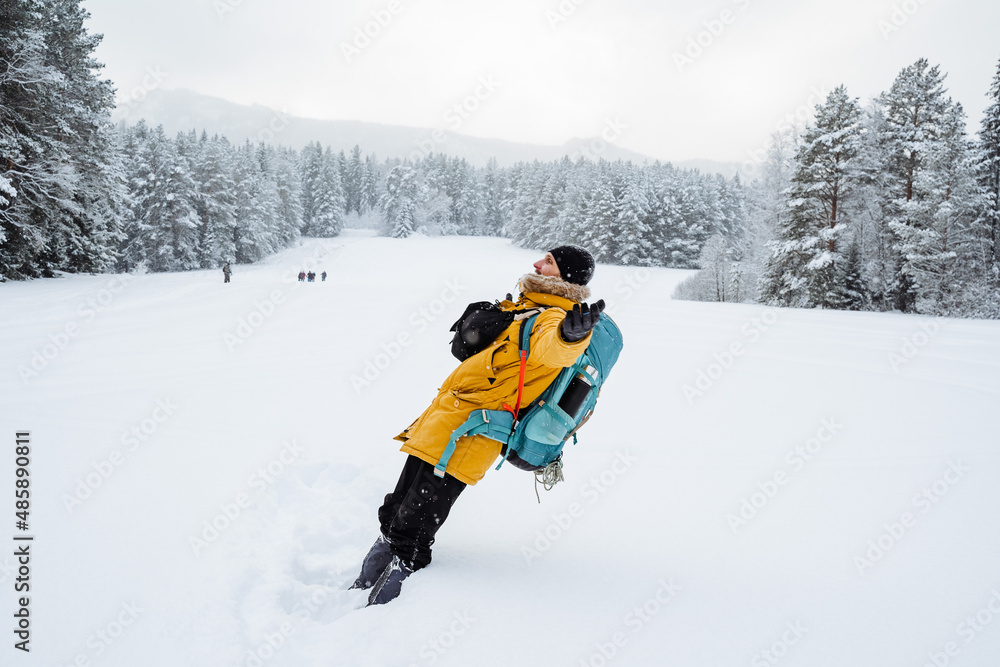 a merry traveler falls into a snowdrift. a hiking backpack on the back of the traveler. Snowy forest and rocks. Climbing the mountain in winter. Survival in the wild. a merry traveler falls into a snowdrift. a hiking backpack on the back of the traveler. Snowy forest and rocks. Climbing the mountain in winter. Survival in the wild.