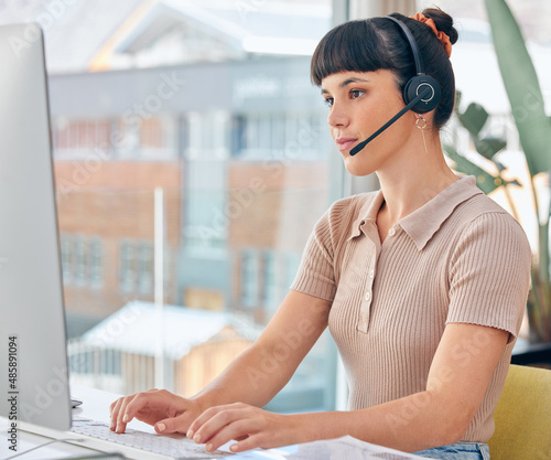 Please hold while I resolve the issue for you. Shot of a woman wearing a headset while working on her computer.
