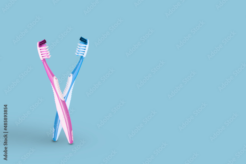 Creative idea made of two toothbrushes pink and blue bristles in an embrace, isolated on light blue background. Creative idea made of two toothbrushes pink and blue bristles in an embrace, isolated on light blue background.