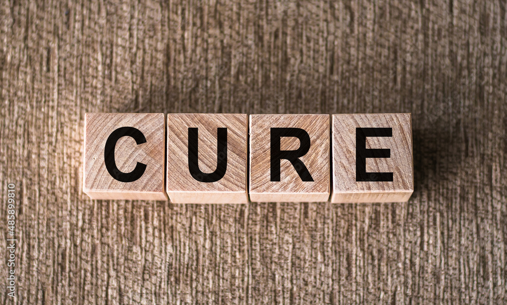 Fototapeta premium Word CURE made of wooden cubes on wooden background. Medical concept of treatment, prevention and side effects.