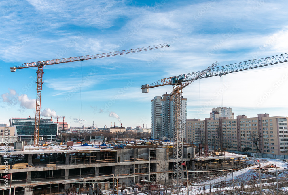Construction cranes at a construction site in the city against the blue sky in winter conditions. The concept of building a new area. Construction of a new building.