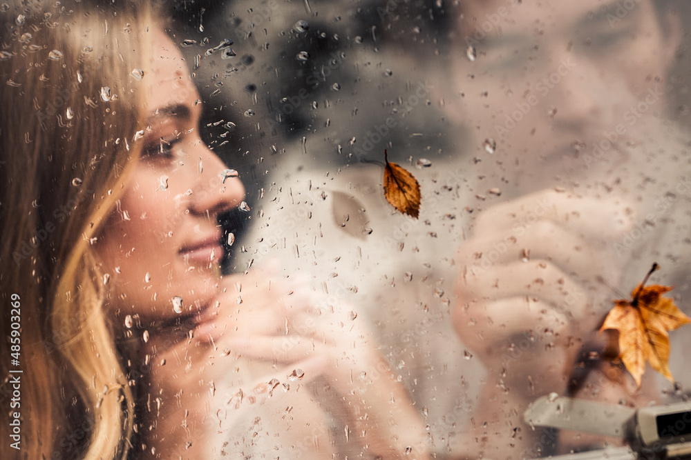 Young happy lovers couple behind wet misted window,rain drops.Drawing heart with finger.Autumn atmosphere,mood,maple leaves.Love romantic road travel. Traveling in camper,house on wheels,trailer