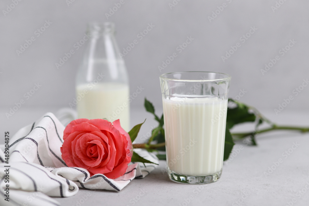 A glass of cow's milk, a bottle and a pink rose on a gray background. Selective focus. A glass of cow's milk, a bottle and a pink rose on a gray background. Selective focus.