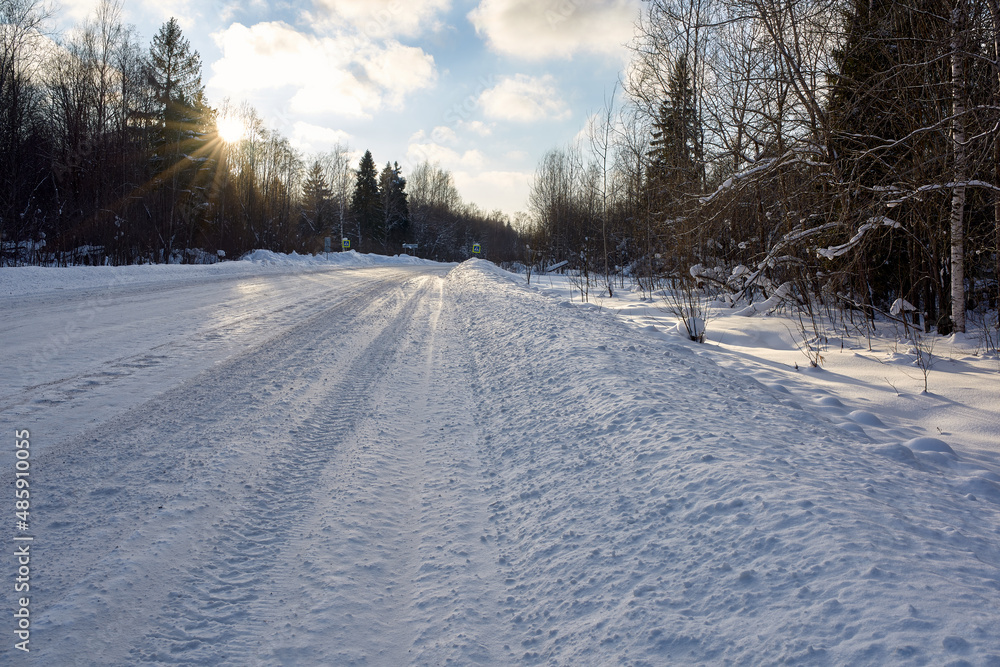 Snow-covered road after harvesting by a tractor, in the rays of sunlight. Snowy Russian winter.