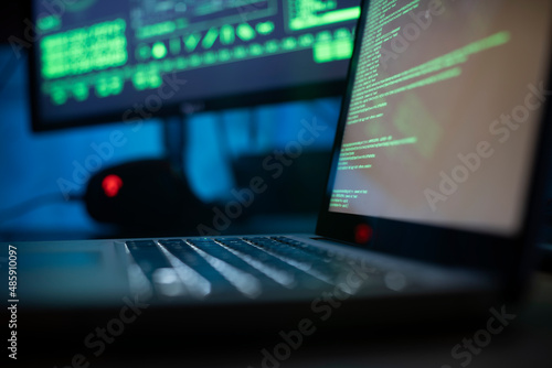 Background image of various computer equipment with programming code on screens on table in dark room, cyber security concept