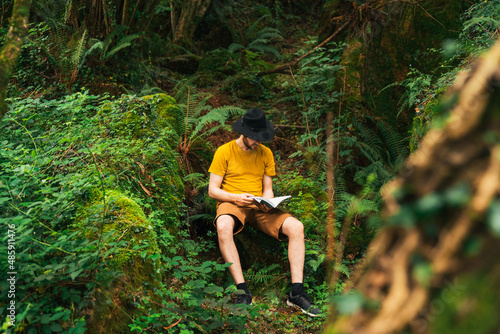 Caucasian man sitting in the middle of the jungle reading a book.