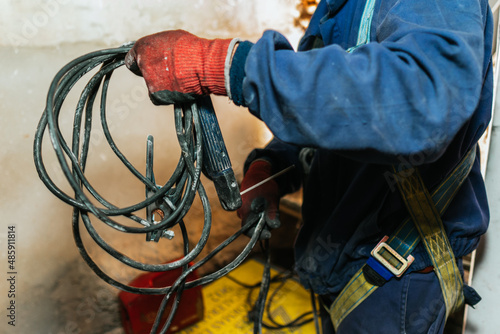 Worker in a blue uniform and red gloves holding a dirty black cable