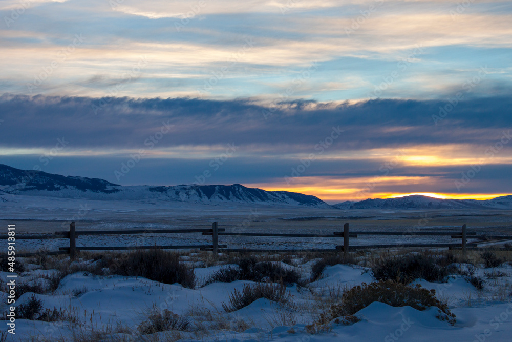 Dramatic sunset across the high plains landscape of Wild West Wyoming, on the path of the Oregon Trail, with winter snow on the hills and a vintage wooden fence