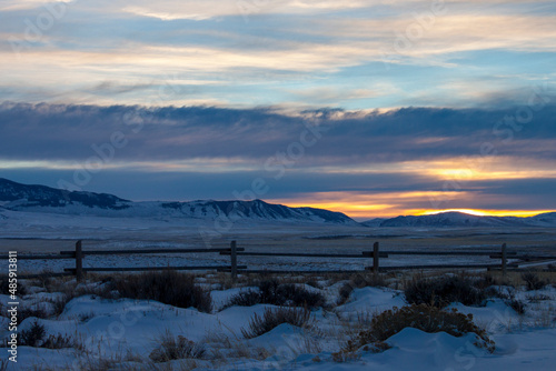 Dramatic sunset across the high plains landscape of Wild West Wyoming  on the path of the Oregon Trail  with winter snow on the hills and a vintage wooden fence