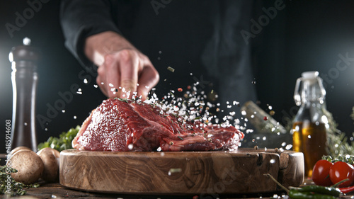 Close-up of falling salt and pepper on tasty beef steak in kitchen, freeze motion.
