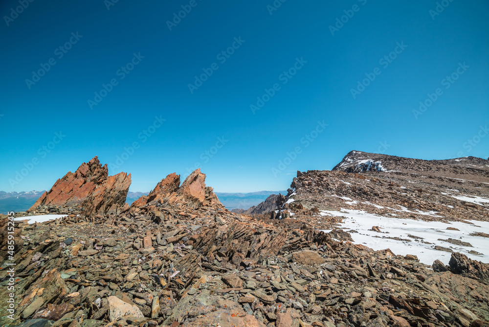 Obraz premium Scenic mountain landscape with old rocks and stones among snow in sunlight. Awesome alpine scenery with stone outliers on high mountain under blue sky in sunny day. Sharp rocks at very high altitude.