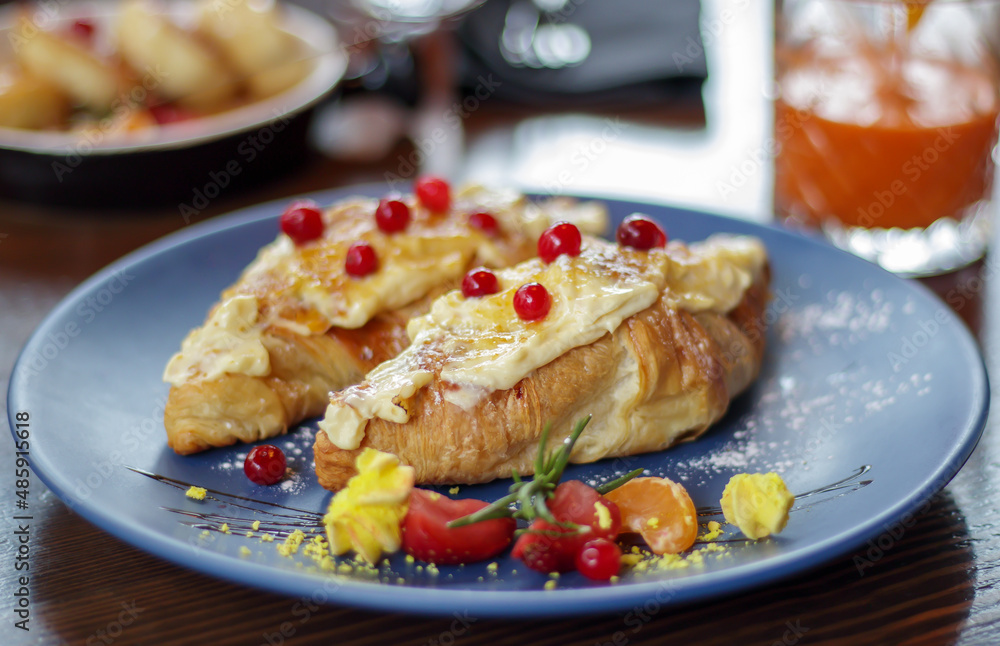 Freshly baked croissants with white, soft and sweet cream, red berries on a plate. Continental breakfast of two delicious croissants with cream on a dark wooden table in a restaurant. Freshly baked croissants with white, soft and sweet cream, red berries on a plate. Continental breakfast of two delicious croissants with cream on a dark wooden table in a restaurant.