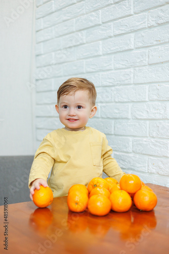 A little boy 2 years old is standing at a table with tangerines. Baby wants to sit down citrus fruits for the first time