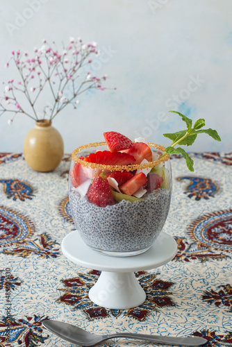 Low angle view of chia pudding dessert with summer berries, strawberries, kiwi and coconut slices, embellished with a mint sprig. No people. photo