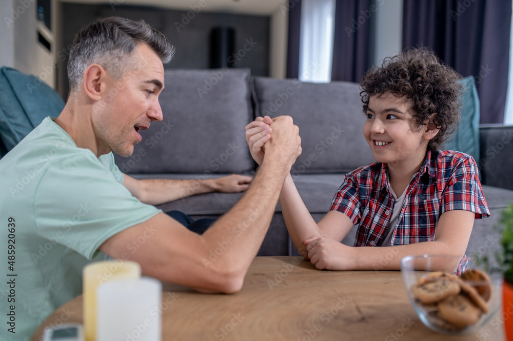 Man and boy sitting at table wrestling on hands Man and boy sitting at table wrestling on hands