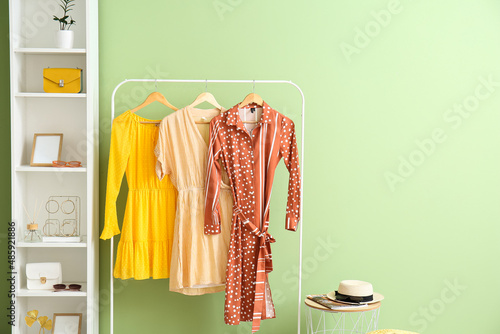 Hanger with dresses and shelf unit with accessories near color wall photo
