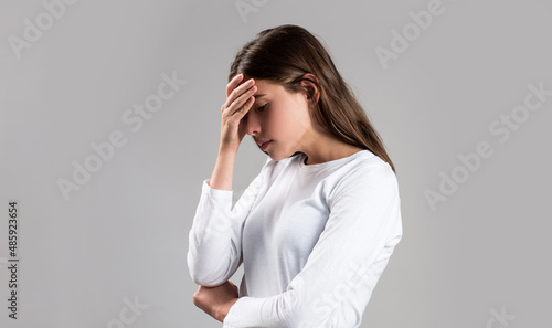 Woman suffering from headache desperate, stressed because pain and migraine. Woman with hard headache holding hands on head. Brunette woman touching her temples feeling stress, on gray background