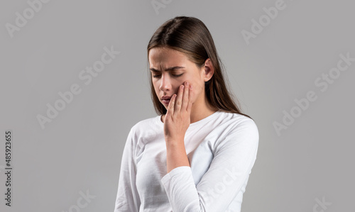 Girl suffering from toothache, tooth decay or sensitivity. Toothache, Woman with Tooth Infection. Woman suffering from toothache against gray background. Young woman suffering from toothache