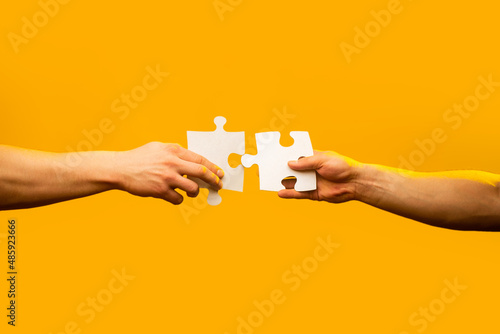 Two hands trying to connect couple puzzle with yellow background. Closeup hands of man connecting jigsaw puzzle. Business solutions, success and strategy concept