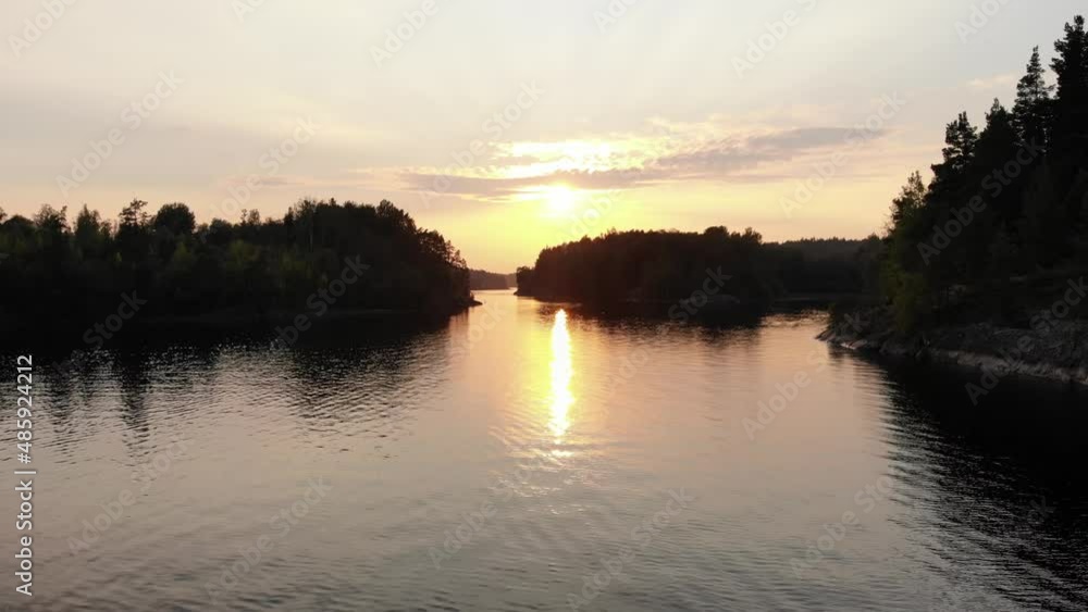 Wild nature of Republic of Karelia, beautiful bay of Ladoga Skerries at sunset. Sail forward across calm water, bright sun shine and dark trees on rocky banks of Murolahti fjord Wild nature of Republic of Karelia, beautiful bay of Ladoga Skerries at sunset. Sail forward across calm water, bright sun shine and dark trees on rocky banks of Murolahti fjord