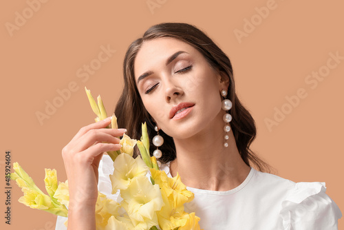 Elegant woman with closed eyes holding bouquet of Gladiolus flowers on color background photo