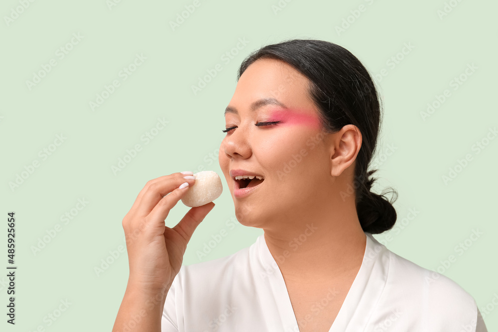 Beautiful Asian woman eating tasty Japanese mochi on color background