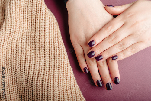 Woman showing her beautiful manicure near a beige wool material. Trendy square nails Manicure. Manicure beauty salon concept. Hands after getting professional manicure in beauty salon, closeup.    