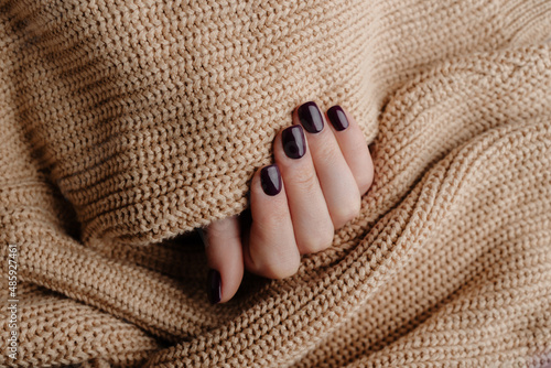 Manicured woman's hand in warm wool beige sweater. Fashionable autumn winter nail design.
Stylish burgundy nails holding knitted wool material. Manicure with gel polish, shellac. Beauty salon concept.