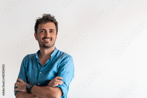 Formal business male portrait. A confident successful casual businessman or manager stands in front of a white background, arms crossed, looking directly at the camera and smiling friendly. High
