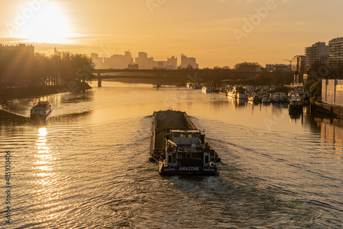 Paris, France - 01 30 2022: Quays of the Seine. View of the freight of a barge sailing along the Seine and The Defense district at sunset from Clichy Bridge photo