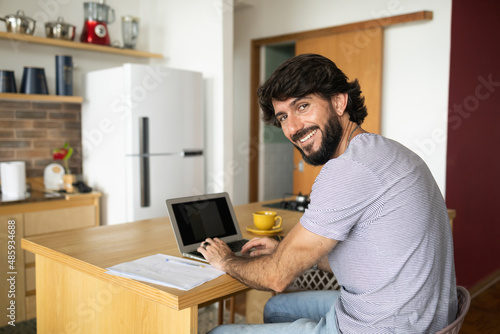 Young business man working at home in his kitchen with laptop and papers on kitchen wooden desk. Home office concept.