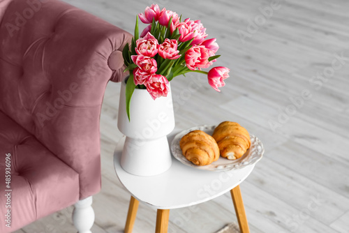 Vase with tulip flowers and plate with croissants on coffee table in living room, closeup